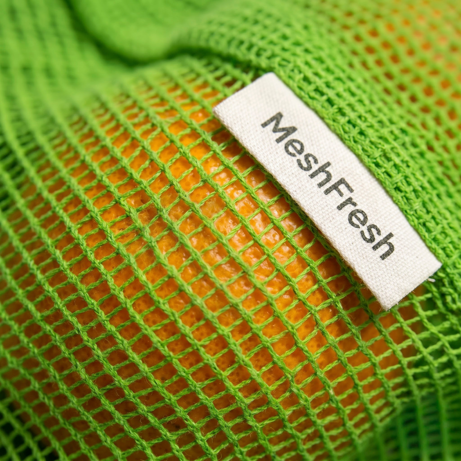 Close-up of the MeshFresh woven label on a green cotton mesh bag holding an orange